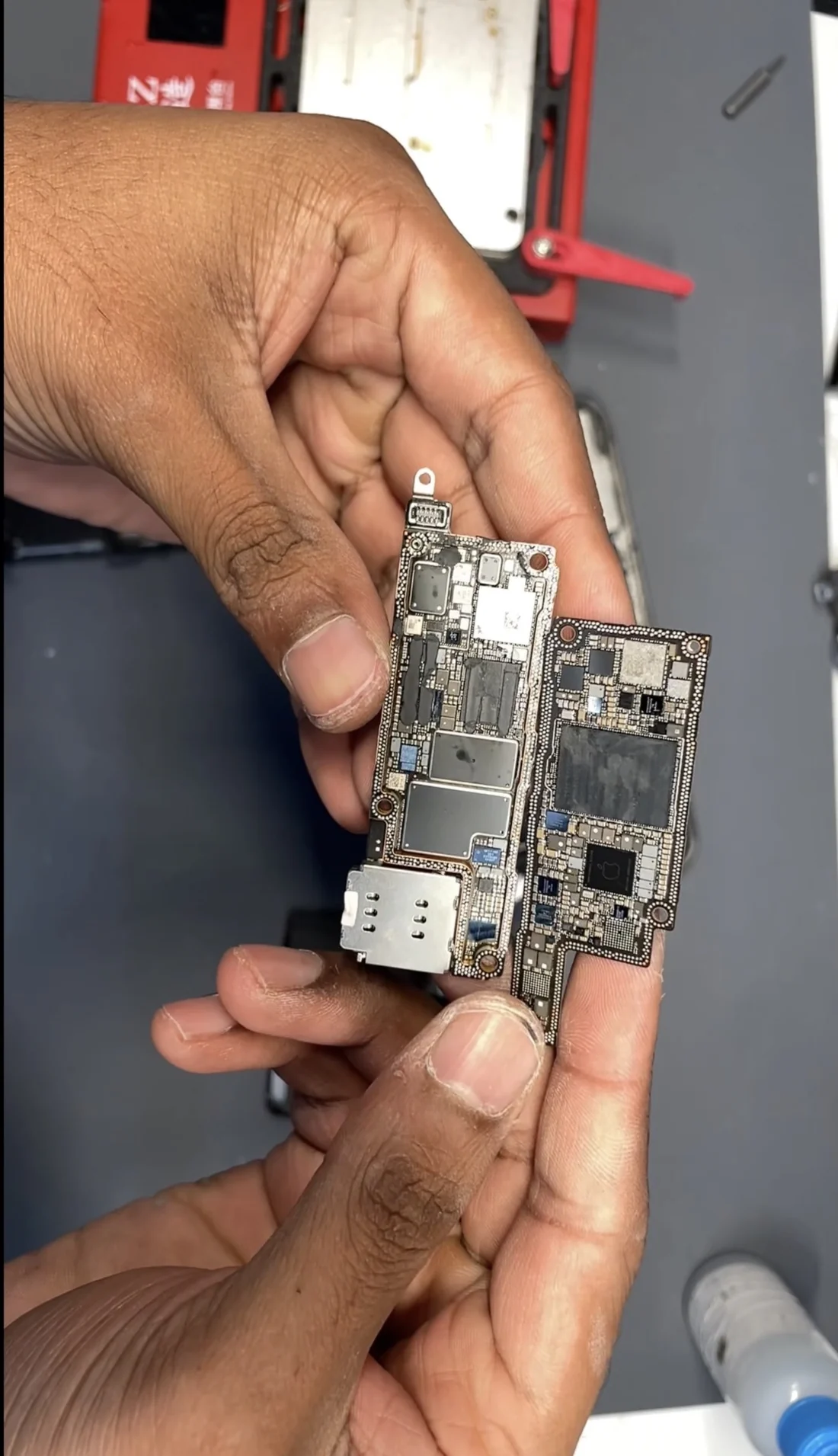 The two halves of an iPhone 14 Pro Max logic board held apart after being separated
