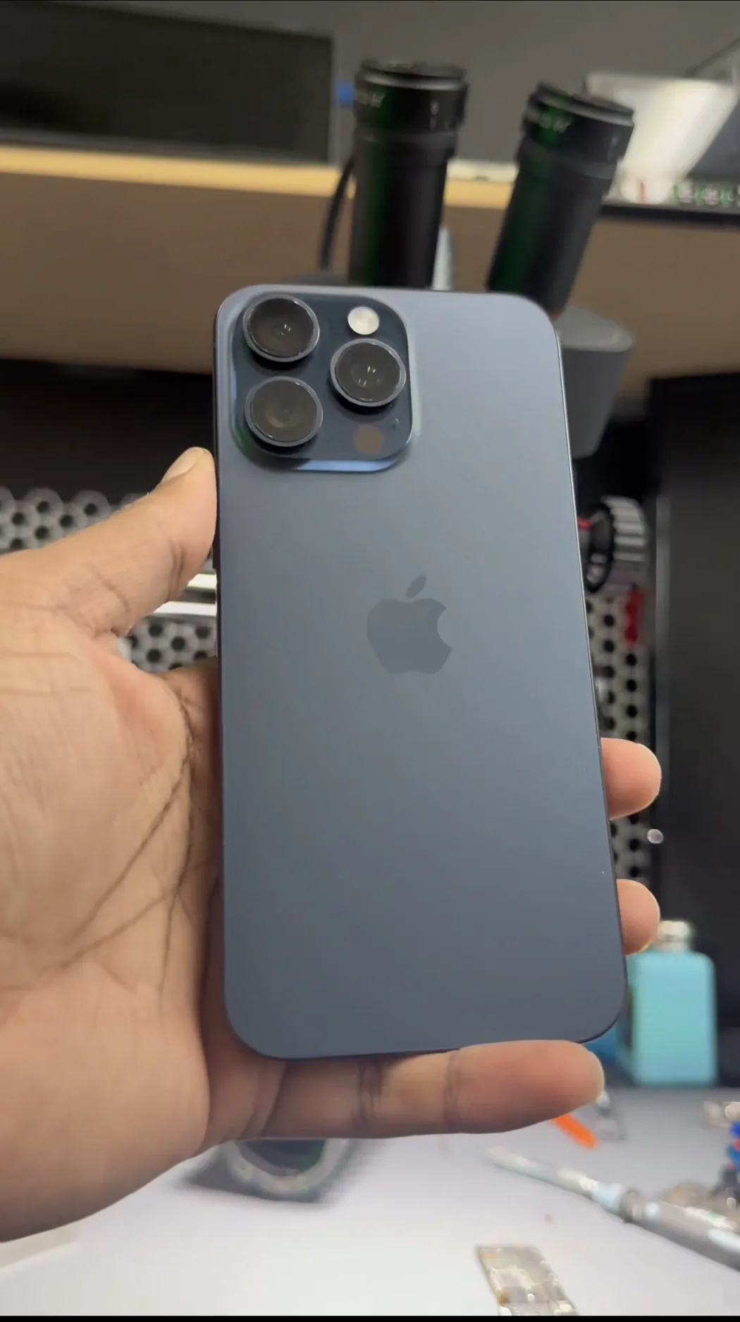 iPhone 15 Pro Max in blue titanium, powered on but showing no display