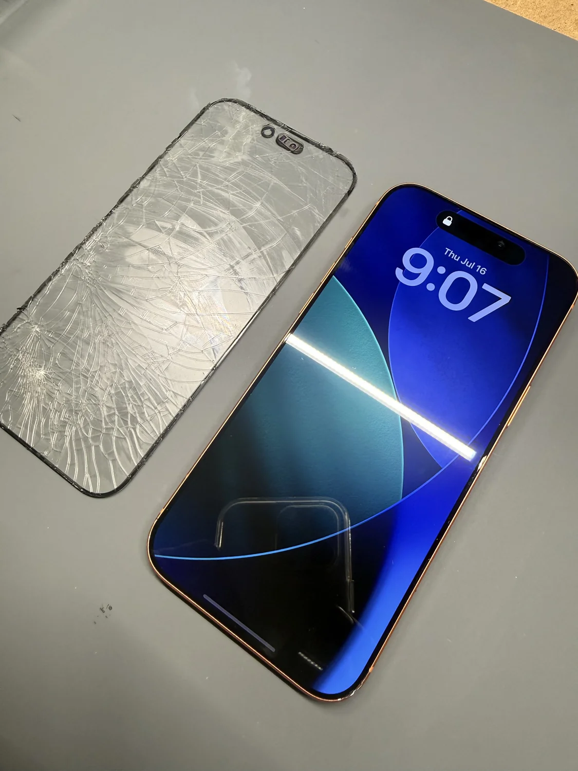 Repaired iPhone 17 Pro Max next to the shattered glass that was removed from it