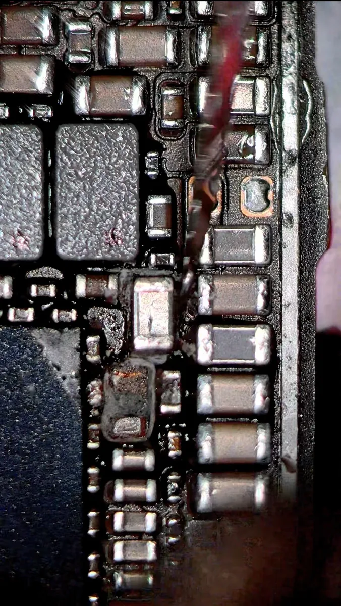 Burnt capacitor and scorched solder mask on an iPhone 14 logic board after a 5V rail short
