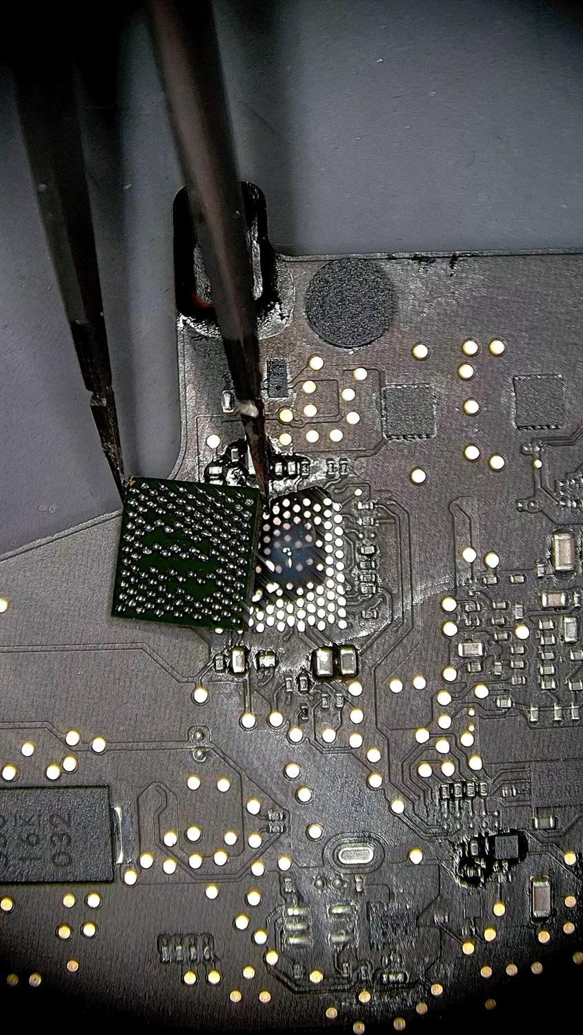 Removing a failed CD3215 power-delivery chip from a MacBook logic board under a microscope