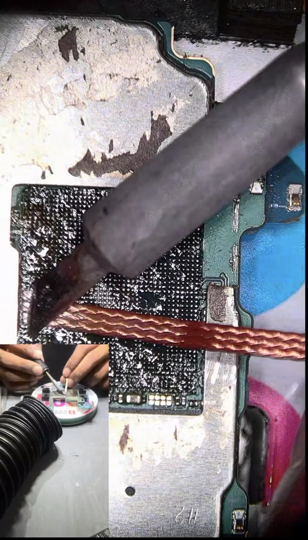 Solder braid and a soldering iron removing old solder from the processor pad array on a Galaxy S23 Ultra board under a microscope